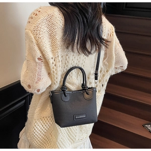 Close-up of black woven tote bag featuring round handles and Fashion metal plaque detail
