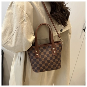 Detail of checkered small bucket bag with golden rivets and adjustable brown shoulder strap