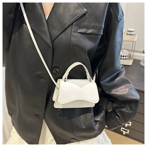 Close-up of white crocodile pattern mini bag worn by model over a black leather jacket