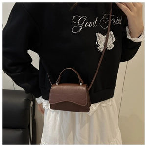 Detail of a brown croc-effect mini crossbody bag featuring a curved top handle and flap design