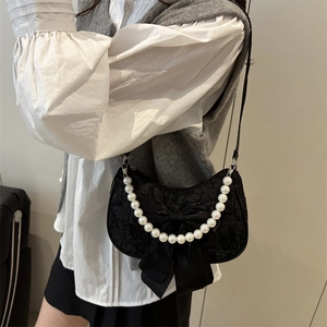 Black lace shoulder bag with large satin bow and white pearl chain strap in a studio setting