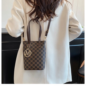 Détail du sac seau vintage à imprimé avec breloque logo M porté par un mannequin