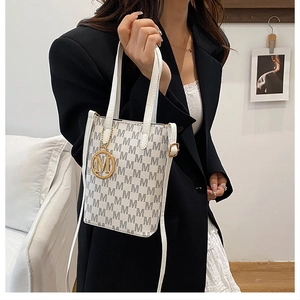 Detail of white mini tote bag with grey M pattern and gold M-shaped hanging metal charm