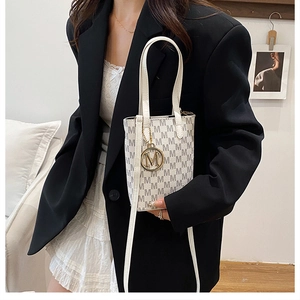 Detail of white vintage tote bag with grey M pattern, gold pendant, and leather texture