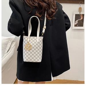 Close-up of white bucket bag featuring grey M-pattern print and gold metallic charm