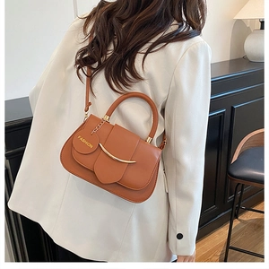 Details der karamellbraunen Satteltasche mit goldener Metallleiste und Mode-Anhänger