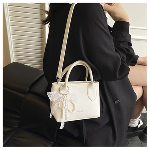 Détail du sac blanc à motif litchi avec breloque nœud en perle et détails argentés