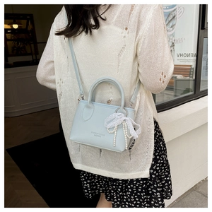 Detail of light blue mini handbag with leather texture, pearl bow and lace pendant