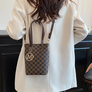 Retro brown bucket bag with monogram print and gold pendant shown on model's shoulder