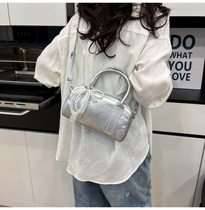 Detail of silver metallic Boston bag with lace pearl bow charm worn as crossbody