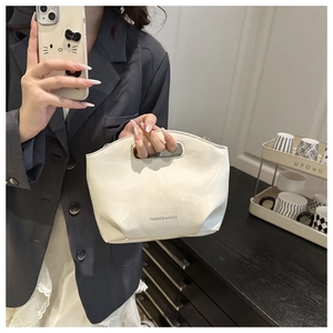 Detail of a minimalist cream-colored semi-circular handbag with an integrated handle