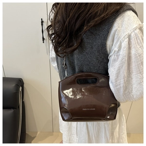 Detail showing high-gloss brown patent leather crossbody bag with white typography text