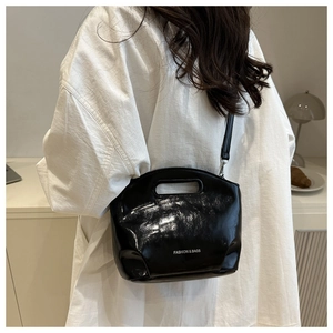Detail of glossy black leather handbag showing white lettering and slim shoulder strap