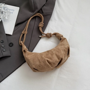 Detail of a brown suede crescent bag with pleated design and knotted strap on white fabric