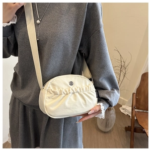 Detail of cream pleated nylon crossbody bag with wide strap worn on a person