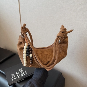 Close-up of brown suede cloud bag featuring wooden bead charms and knotted strap detail