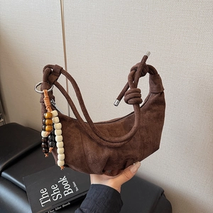 Detail of dark brown faux suede crescent bag with knotted handle and beaded ornament