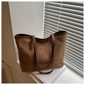 Detail of a brown suede tote bag with leather trim and logo patch on a minimalist ledge