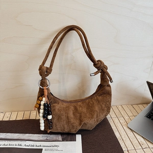 Detailed view of brown suede pleated half-moon bag with knot strap and beaded charm
