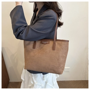 Detail of a brown suede tote bag featuring a leather brand tag and sleek carry handles