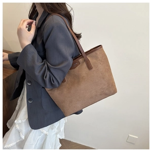Detail of brown faux suede tote bag featuring leather straps and premium brand logo patch
