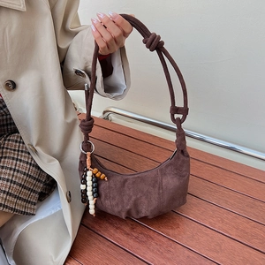 Detail of dark brown suede crescent bag featuring stylish bead pendant and knotted strap