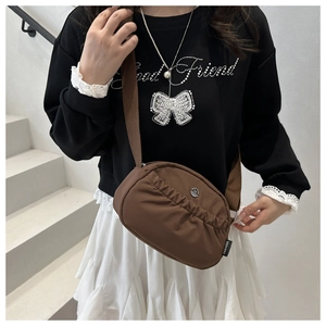 Detail of a brown waterproof nylon crossbody bag featuring pleated design and side brand label