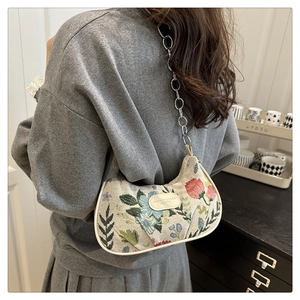 Detailed shot of floral embroidered crescent bag with silver chain on model's shoulder