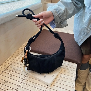 Detail of black pleated croissant bag with thick knotted handle and wooden bead tassel