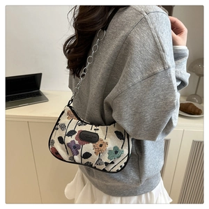 Detail of floral embroidery on cream canvas bag with black leather trim and chain strap