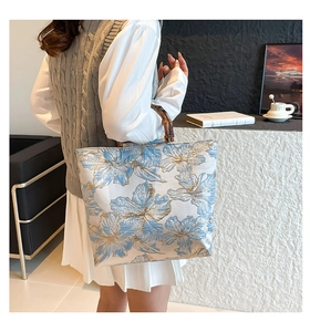 Detail of floral jacquard tote bag with natural bamboo handles held by a model