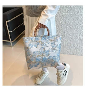 Detail of bamboo handles on floral tote bag with blue patterns and gold outline