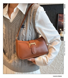 Detailed close-up of brown leather underarm bag with an elegant golden metal buckle clasp
