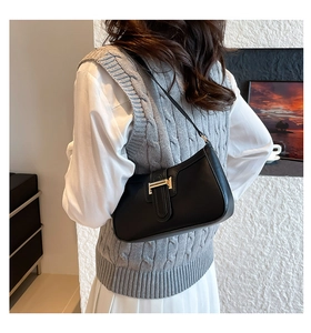 Close-up of a black leather underarm bag with gold buckle worn on a model's shoulder