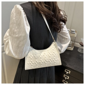 Close-up of white crescent underarm bag with quilted texture worn by model in a street setting