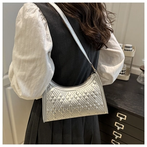 Detail of silver quilted texture on a stylish underarm bag worn by a model in a room