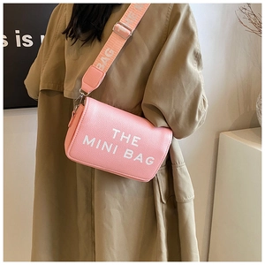 Detail of pink crossbody bag with THE MINI BAG text and stylish woven shoulder strap