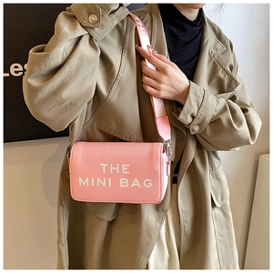 Pink mini crossbody bag with wide logo strap shown on a model in a beige trench coat