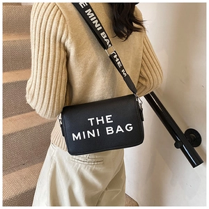 Detail of black pebbled leather mini bag with wide logo strap worn by a model