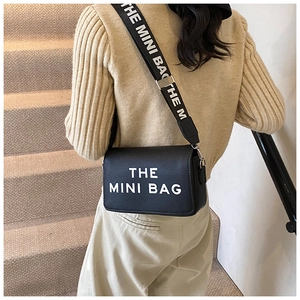 Detail of black crossbody bag with wide shoulder strap and white letter print on model
