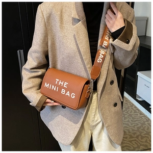 Detail of brown leather mini bag with wide lettered strap and The Mini Bag text