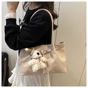 Shoulder view of beige woven tote bag with a small bear charm and buckle detail