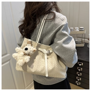 Close-up of cream woven tote bag featuring a plush puppy charm and braided texture details