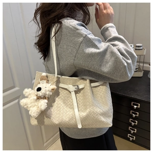 Detail of light beige woven leather tote bag with white plush bear pendant and silver buckle