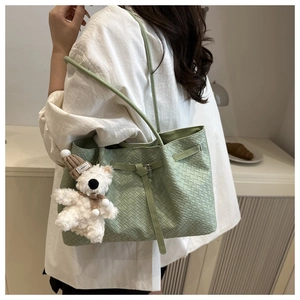Close-up of green woven bucket bag featuring a cute plush bear charm and thin strap
