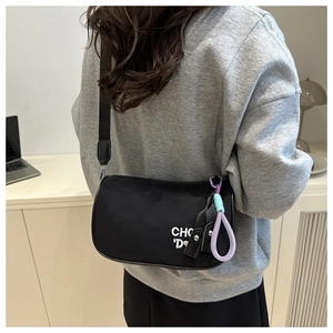 Detail of black nylon crossbody pillow bag featuring a stylish woven colorful charm