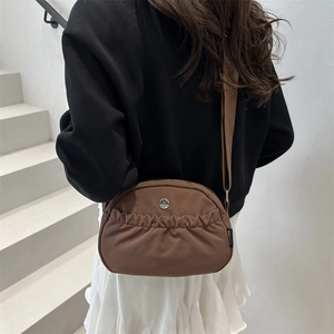 Brown minimalist nylon crossbody bag with pleated pocket and adjustable strap on model