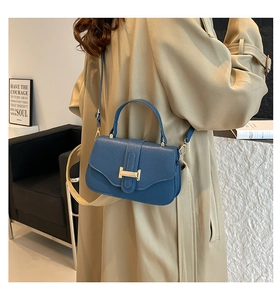 Detail of blue lychee leather handbag with gold H clasp and top handle on beige coat