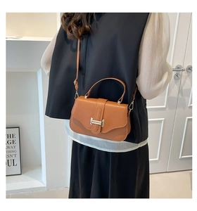 Detail of a brown leather shoulder bag featuring a metallic H buckle and top handle