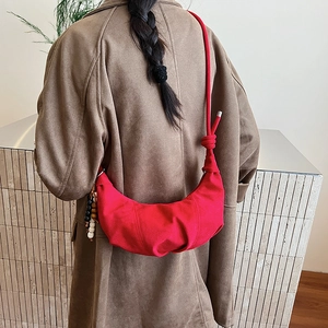 Red crescent-shaped crossbody cloud bag with knot strap and colorful beaded charm detail